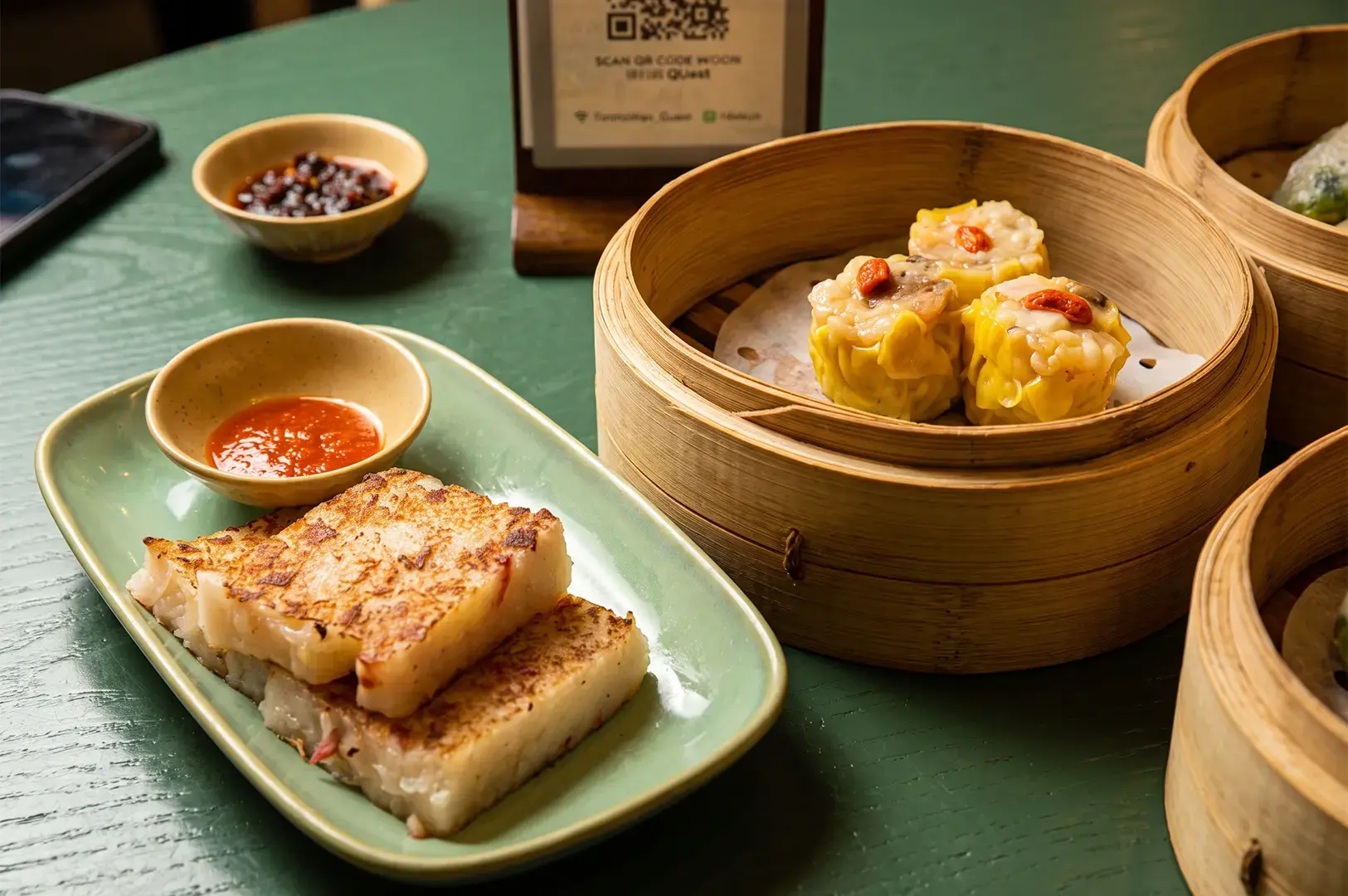 Tim Ho Wan signature dishes Pork and Shrimp Dumplings and Fried Radish Cake served on bamboo steamers and a green rectangular platter.