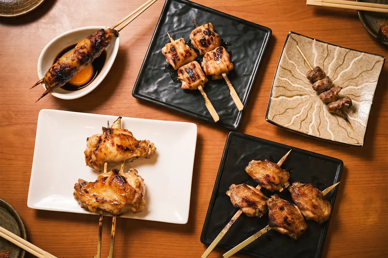 A variety of chicken part skewers served on black and white platters arranged on a wooden table.