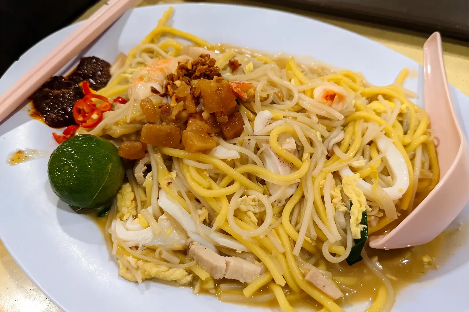A zoomed in view of a fried hokkien mee on a white plate with chopsticks.