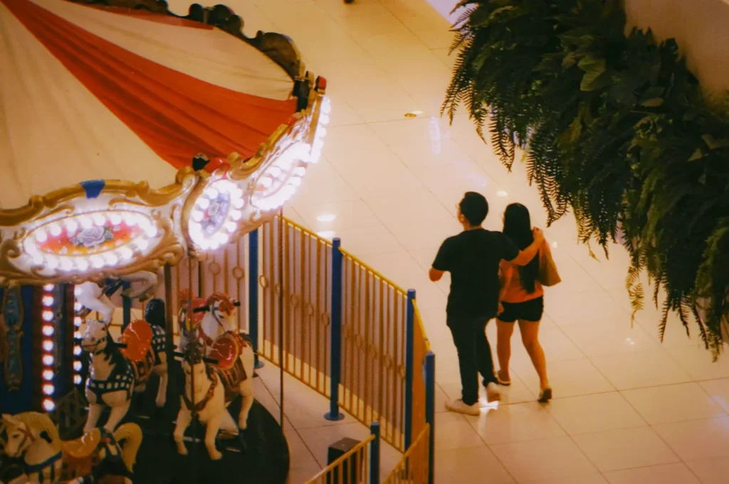 A couple walking through a mall beside a carousel.