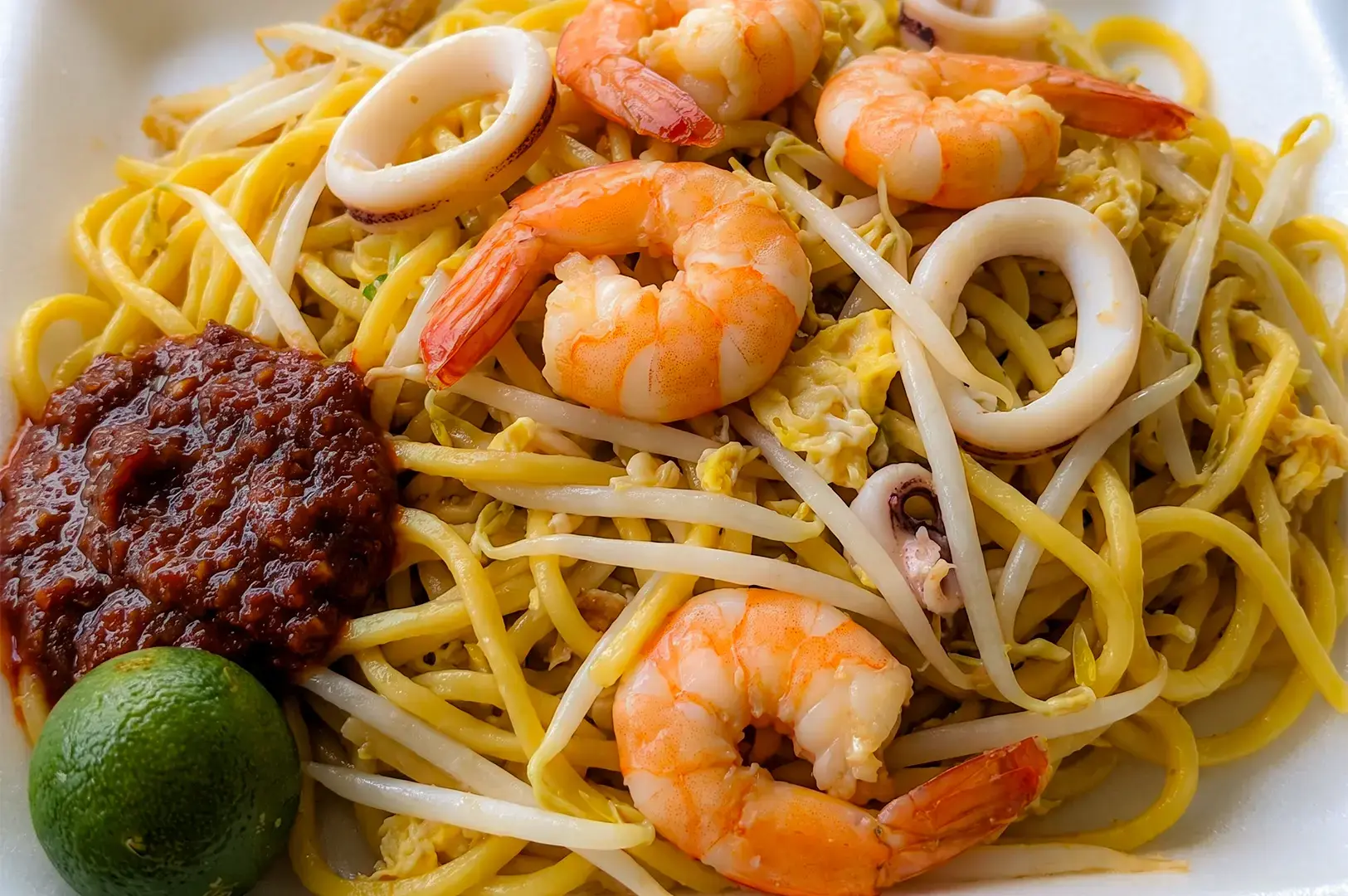 A close up view of a hokkien mee bowl with seafood topped on fried noodles.
