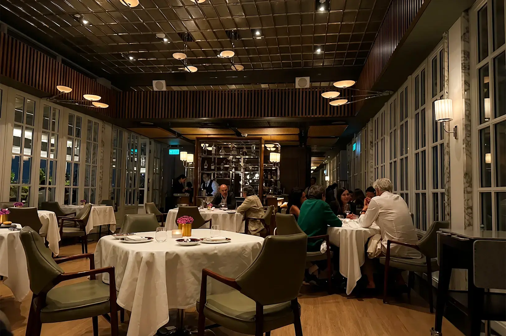 Spago Dining Room at dusk with a dim and warmly lit interior and customers dining at tables with white cloth.
